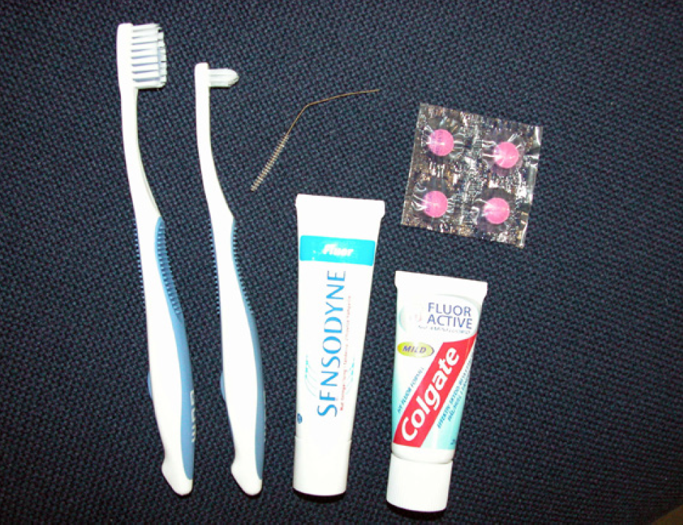 på billedet ses forskellige typer tandbørster, tandpasta og røde farvetabletter